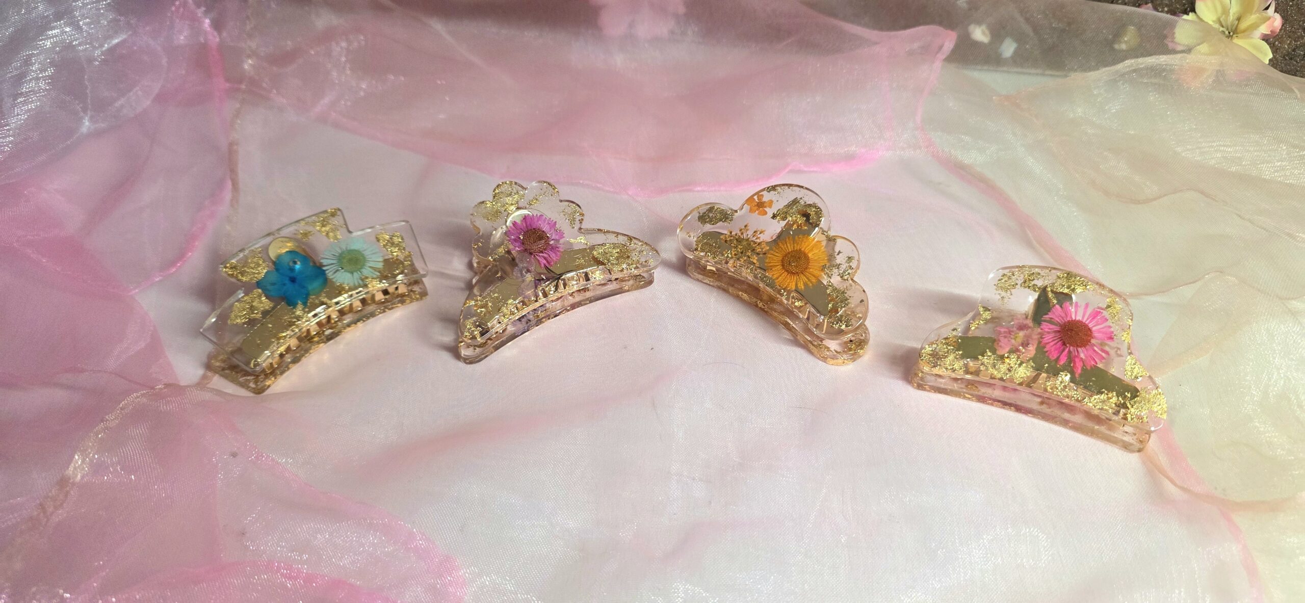 Verschiedene handgefertigte Haarklammern aus Epoxidharz in der Übersicht – Edle Designs mit bunten echten Blüten und glänzendem Blattgold von Traumharz.