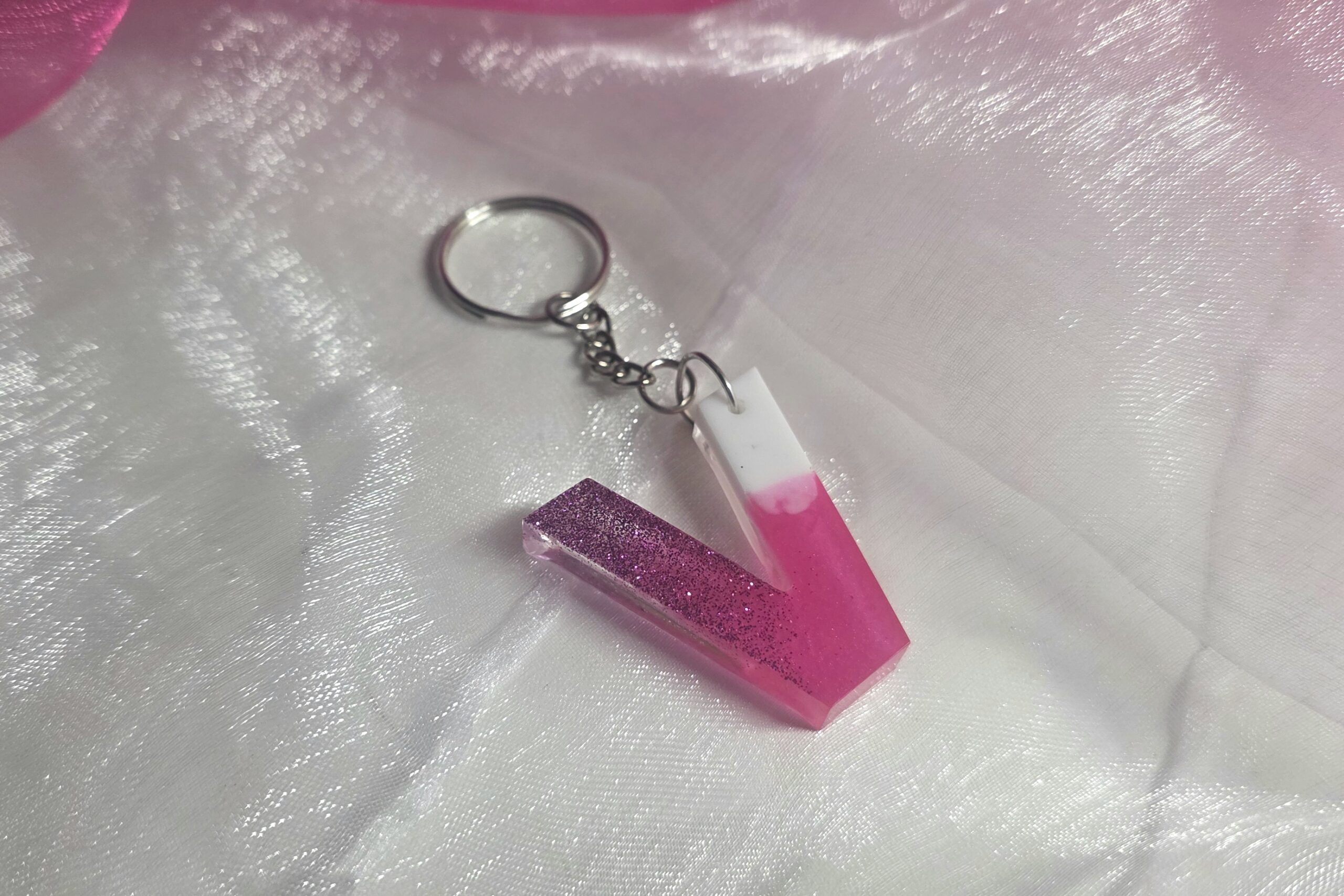 Handgefertigter Buchstaben-Schlüsselanhänger (Buchstabe V) aus Epoxidharz im edlen Farbverlauf Pink-Weiß mit glänzendem Finish und silbernem Ring.