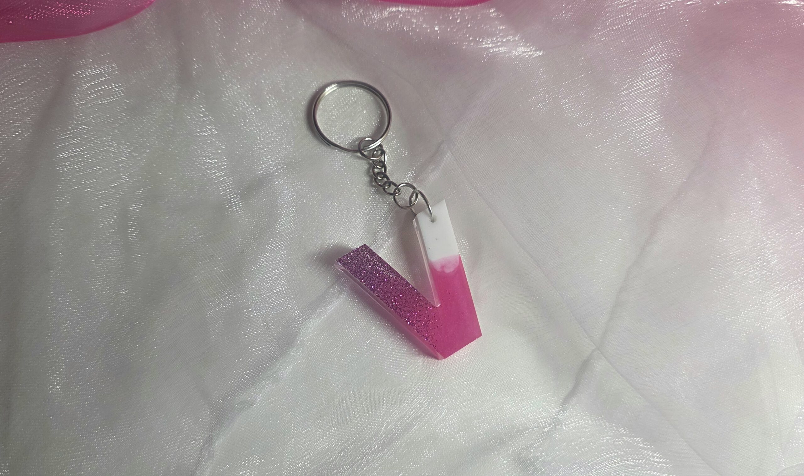 Handgefertigter Buchstaben-Schlüsselanhänger (Buchstabe V) aus Epoxidharz im edlen Farbverlauf Pink-Weiß mit glänzendem Finish und silbernem Ring.