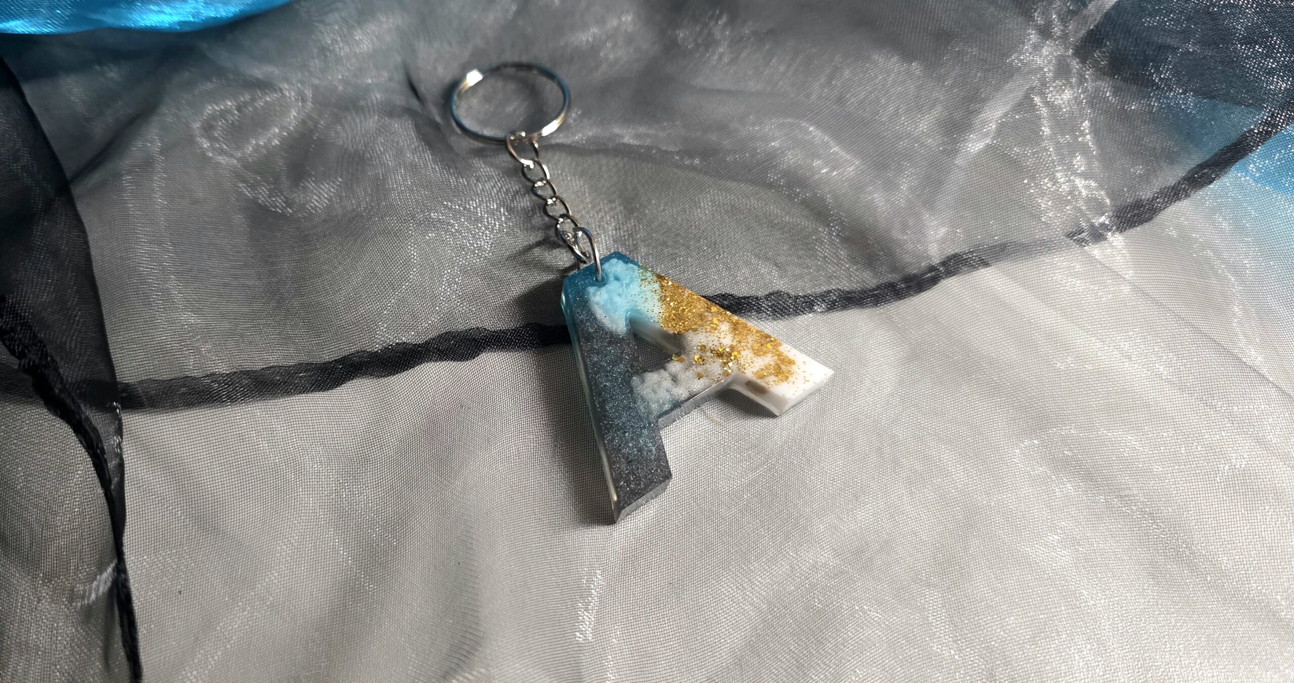 Handgefertigter Buchstaben-Schlüsselanhänger (Buchstabe A) aus Epoxidharz – Einzigartiges Unikat im Petrol-Schwarz-Weiß-Design mit edlen Metallic-Effekten und silberner Kette von Traumharz.