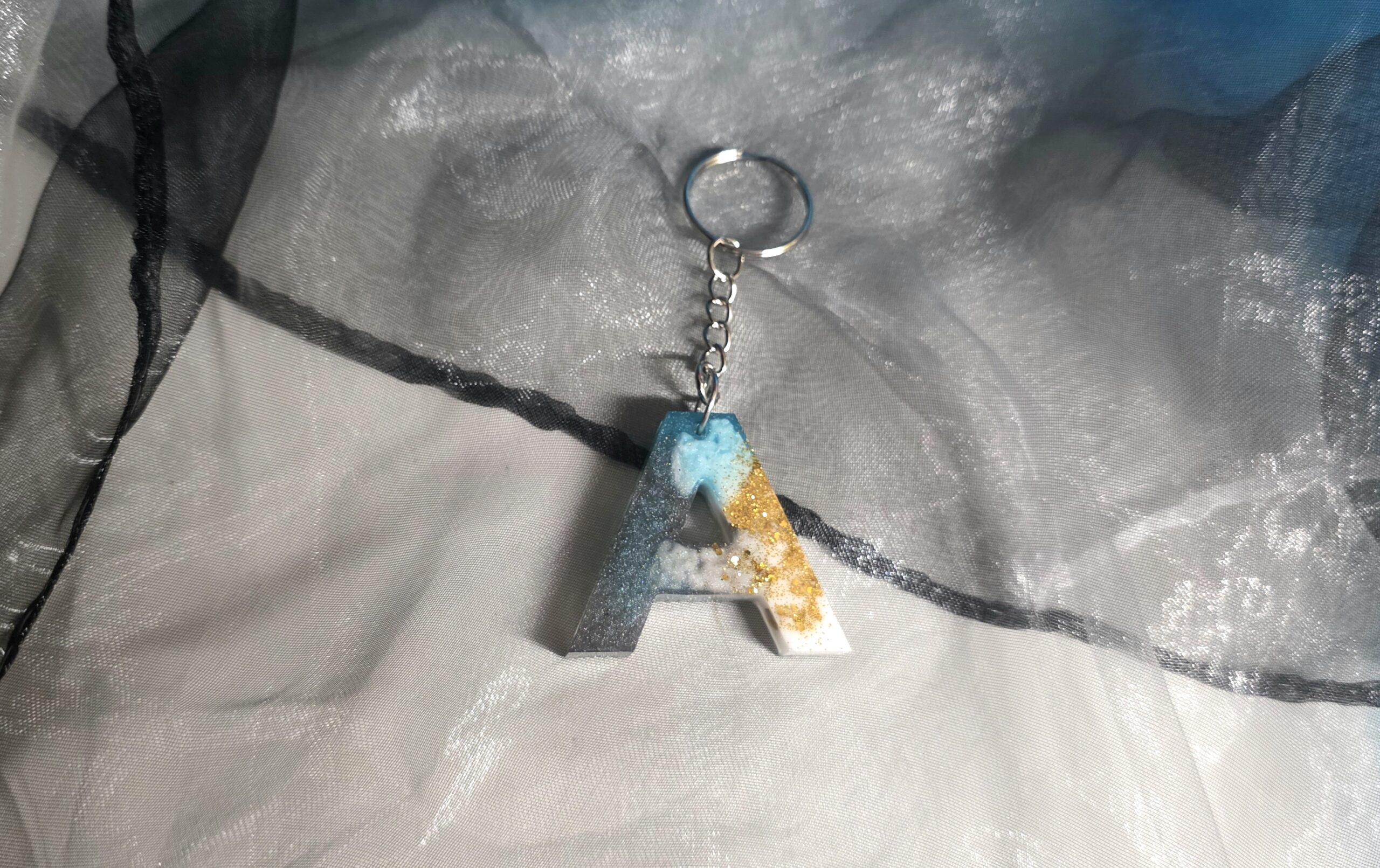 Handgefertigter Buchstaben-Schlüsselanhänger (Buchstabe A) aus Epoxidharz – Einzigartiges Unikat im Petrol-Schwarz-Weiß-Design mit edlen Metallic-Effekten und silberner Kette von Traumharz.