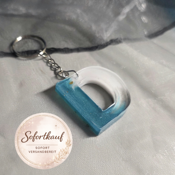 Hauptbild (Türkis-Weiß): Handgefertigter Buchstaben-Schlüsselanhänger (Buchstabe D) aus Epoxidharz im frischen Türkis-Weiß-Verlauf mit silberner Kette und Schlüsselring von Traumharz.