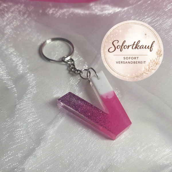 Handgefertigter Buchstaben-Schlüsselanhänger (Buchstabe V) aus Epoxidharz im edlen Farbverlauf Pink-Weiß mit glänzendem Finish und silbernem Ring.